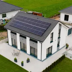 Nowoczesny biały dom z panelami słonecznymi na dachu, otoczony zielonym trawnikiem i patio.