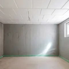 Pusta piwnica z betonowymi ścianami i sufitem podwieszanym. Okno wpuszcza światło. Zastanawiasz się, ile kosztuje remont piwnicy?