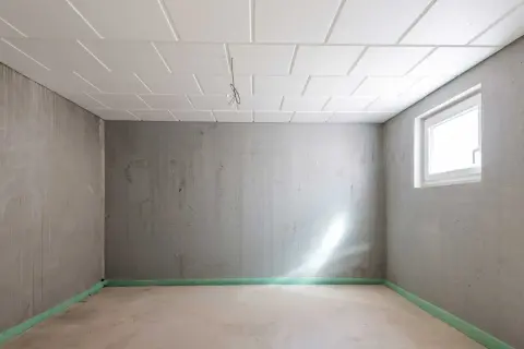 Pusta piwnica z betonowymi ścianami i sufitem podwieszanym. Okno wpuszcza światło. Zastanawiasz się, ile kosztuje remont piwnicy?