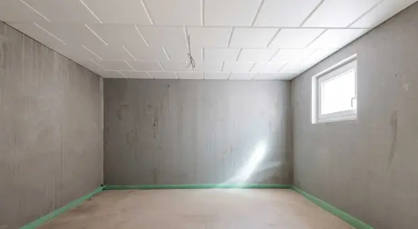 Pusta piwnica z betonowymi ścianami i sufitem podwieszanym. Okno wpuszcza światło. Zastanawiasz się, ile kosztuje remont piwnicy?
